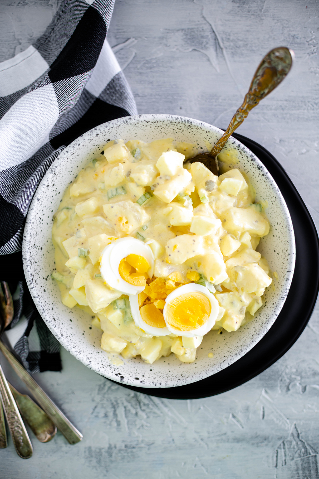 White bowl filled with potato salad. Set on top of a black plate.