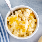 White bowl filled with macaroni and cheese with blue and white striped napkin to the left.