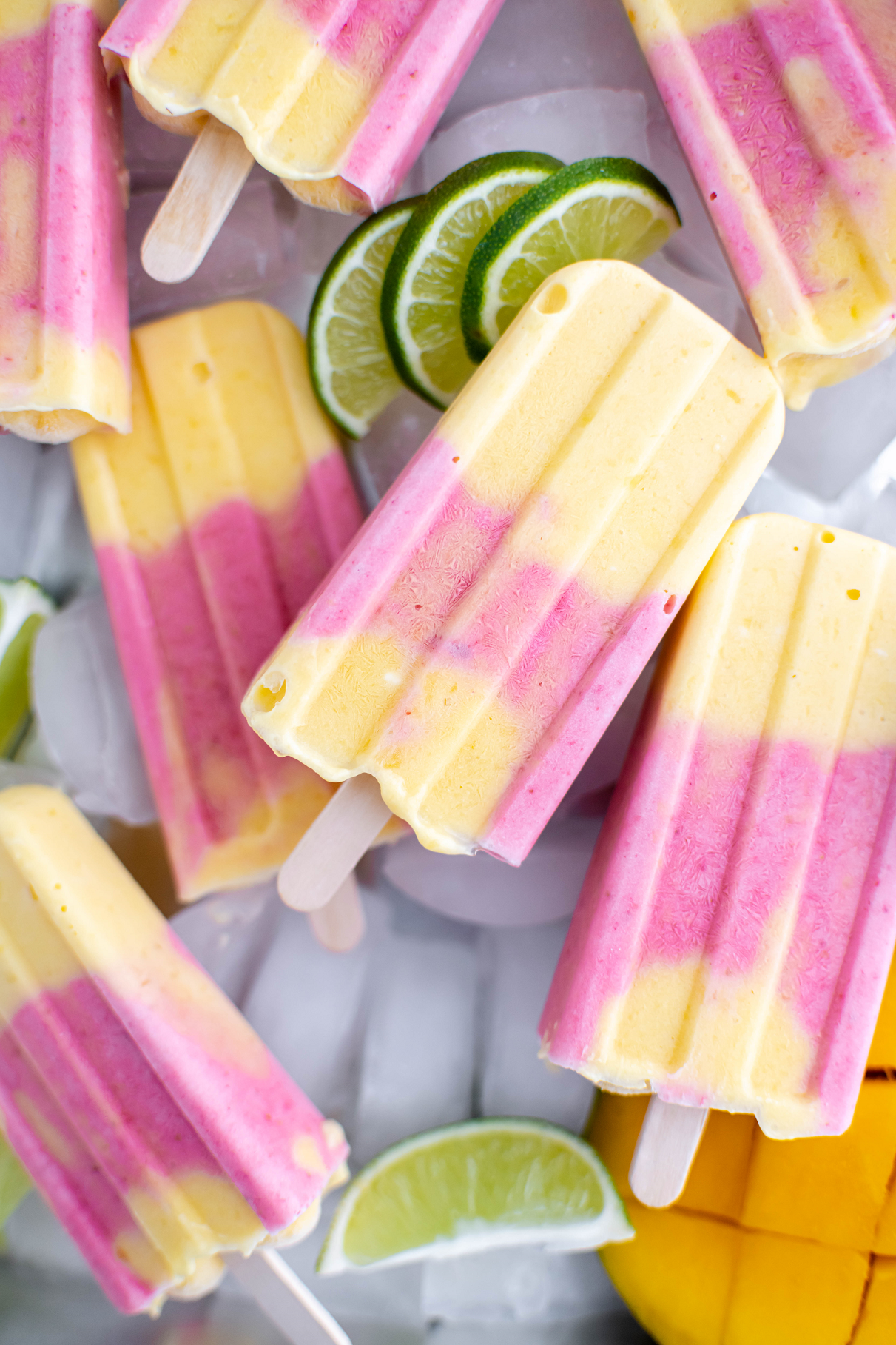 Layer of ice cubes topped with strawberry mango popsicles. Garnish of lime slices and half a mango.