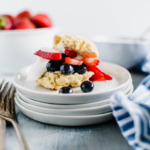 Shortcake fille with blueberries and strawberries and a dollop of whipped cream. Bowl of strawberries in the background.