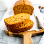 Loaf of pumpkin bread on wooden board. Two thick slices cut and in forefront.