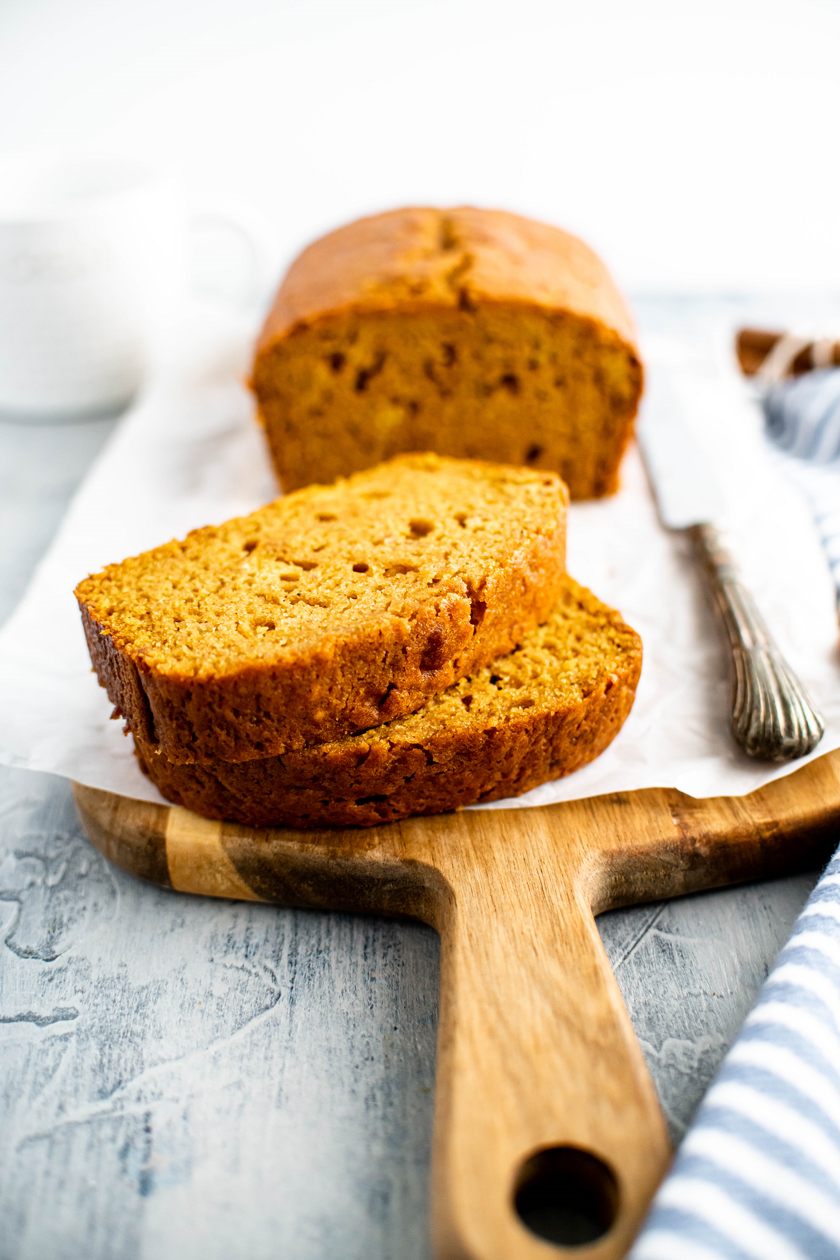 Loaf of pumpkin bread on wooden board. Two thick slices cut and in forefront.