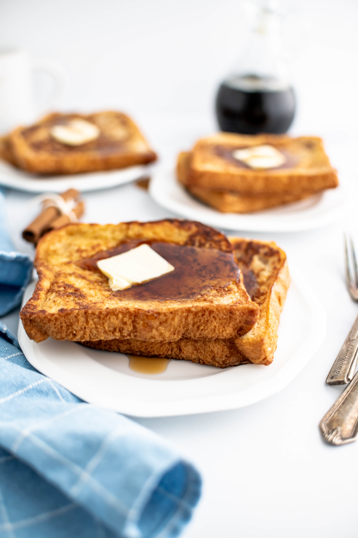 Three small white plates, each with two pieces of spiced french toast topped with butter and maple syrup.