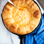 Cast iron skillet filled with Rhodes rolls and buffalo chicken dip in the middle.