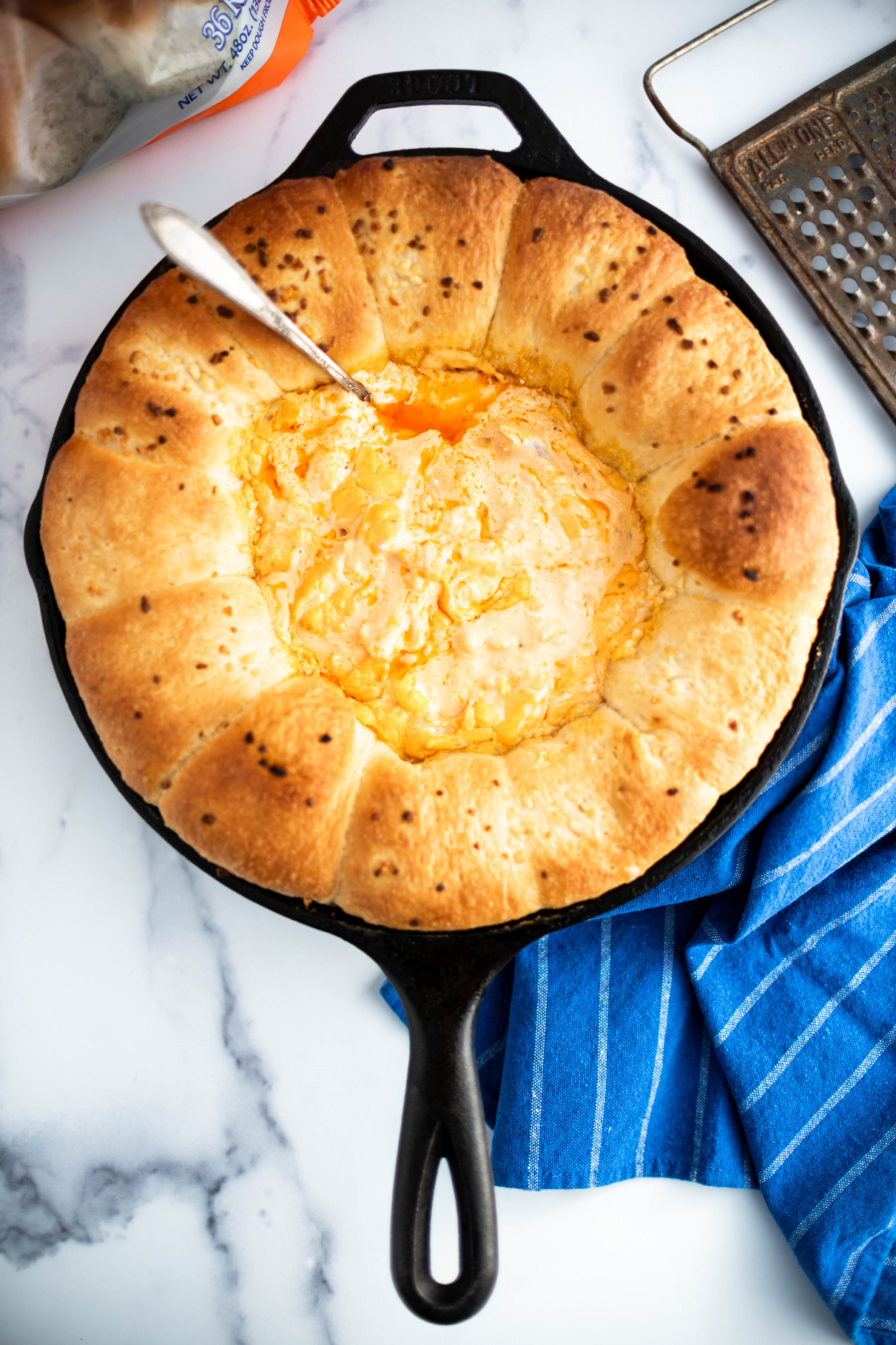 Cast iron skillet filled with Rhodes rolls and buffalo chicken dip in the middle.