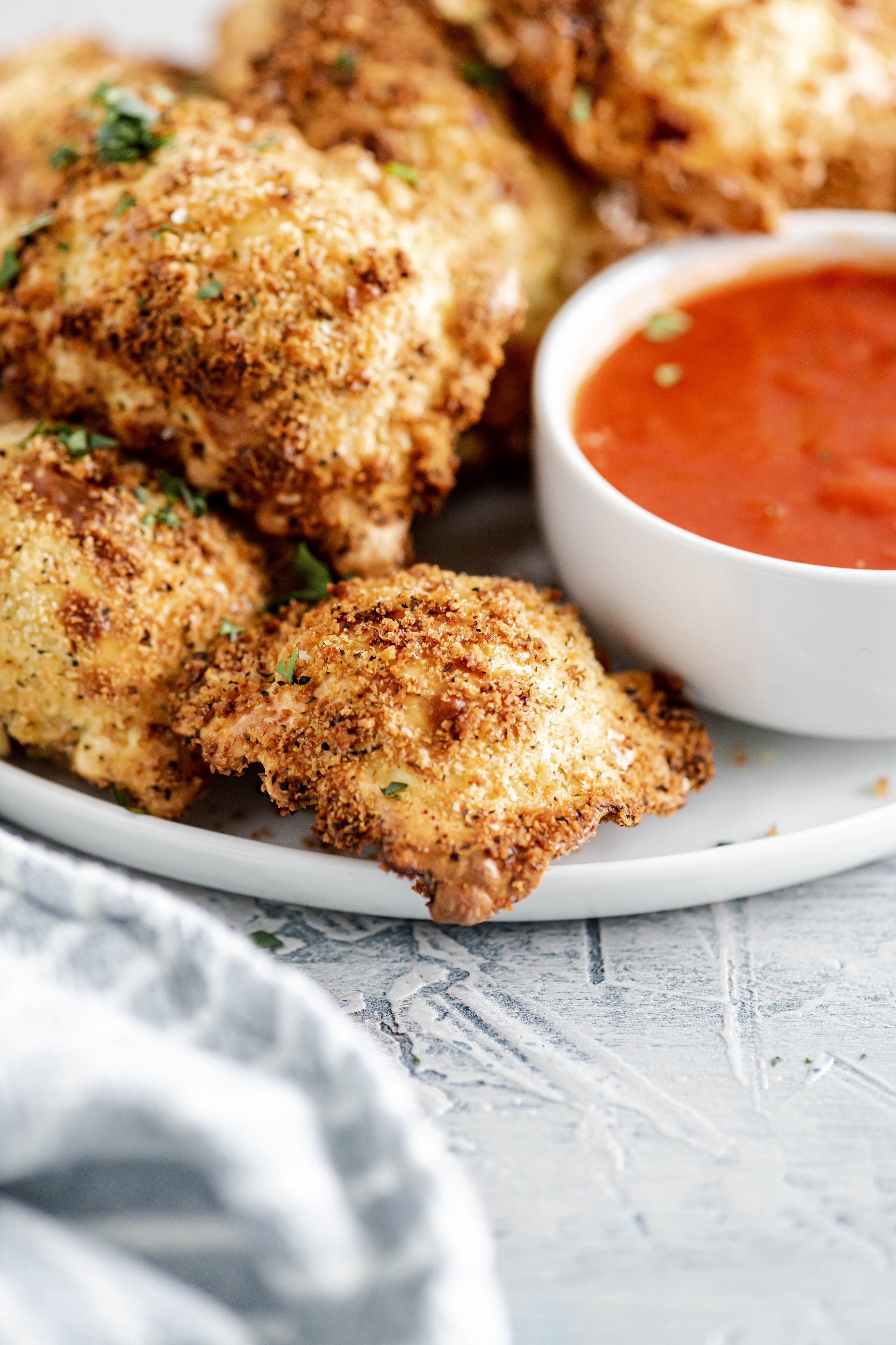 White round plate filled with air fryer ravioli and a small white round bowl filled with marinara sauce.