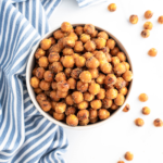 Big bowl of chiptole ranch pretzel rounds. Some scattered around the bowl and a blue and white striped kitchen towel on the side of the bowl.