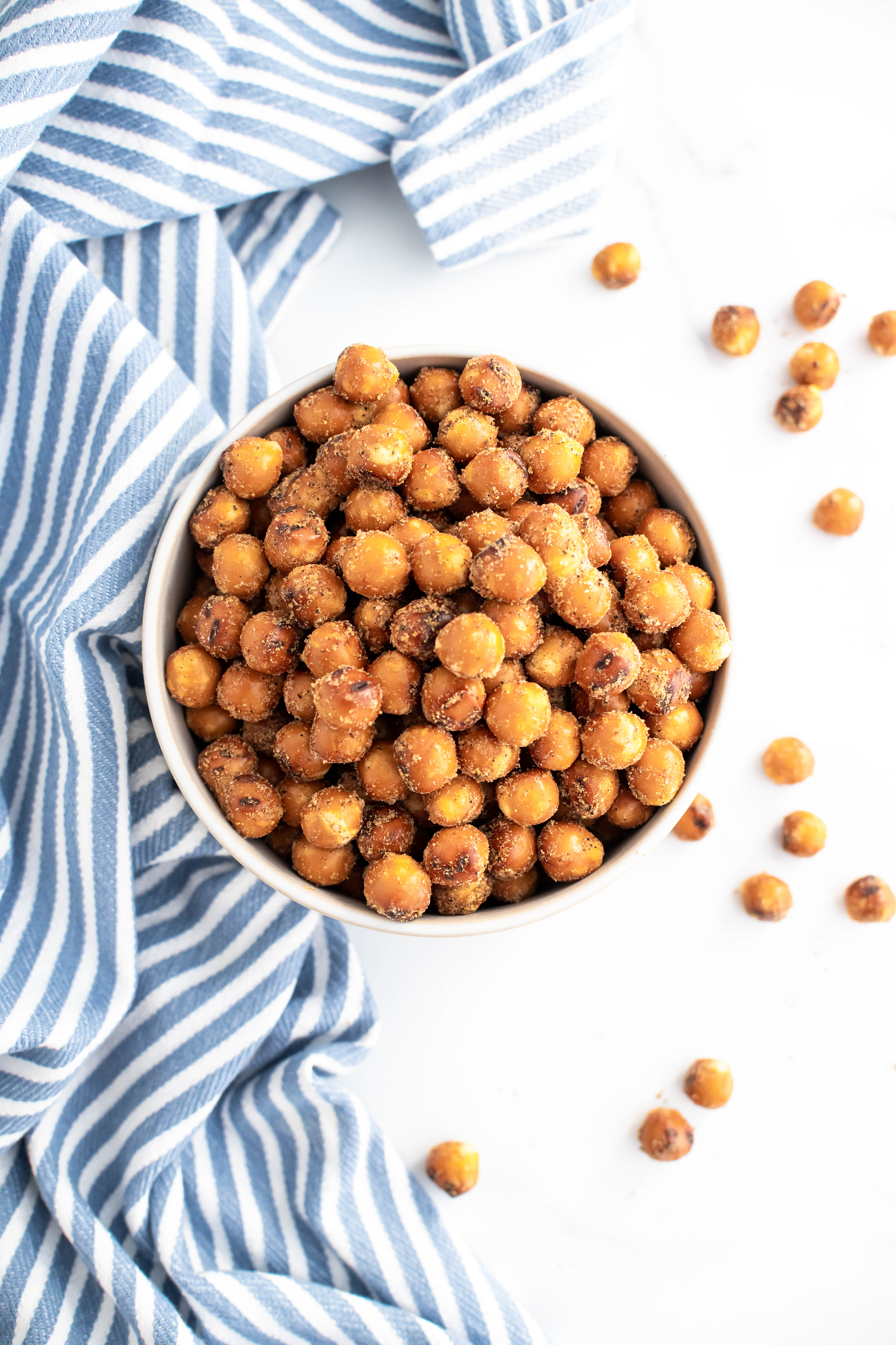 Big bowl of chiptole ranch pretzel rounds. Some scattered around the bowl and a blue and white striped kitchen towel on the side of the bowl.