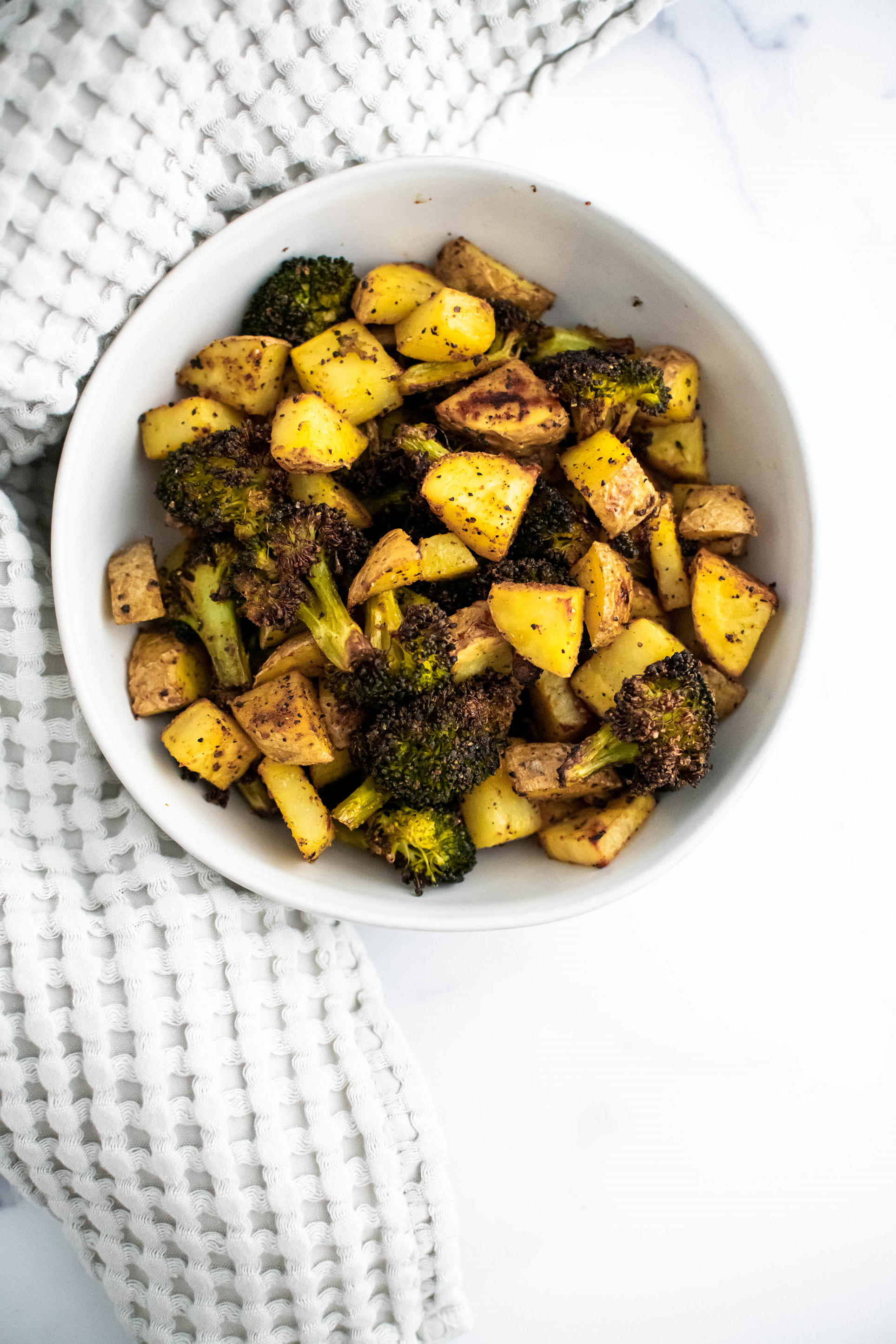 White round bowl filled with roasted potatoes and broccoli.