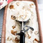 Loaf pan filled with cinnamon roll ice cream. Vintage ice cream scoop with a scoop of ice cream in it leaning in the pan.