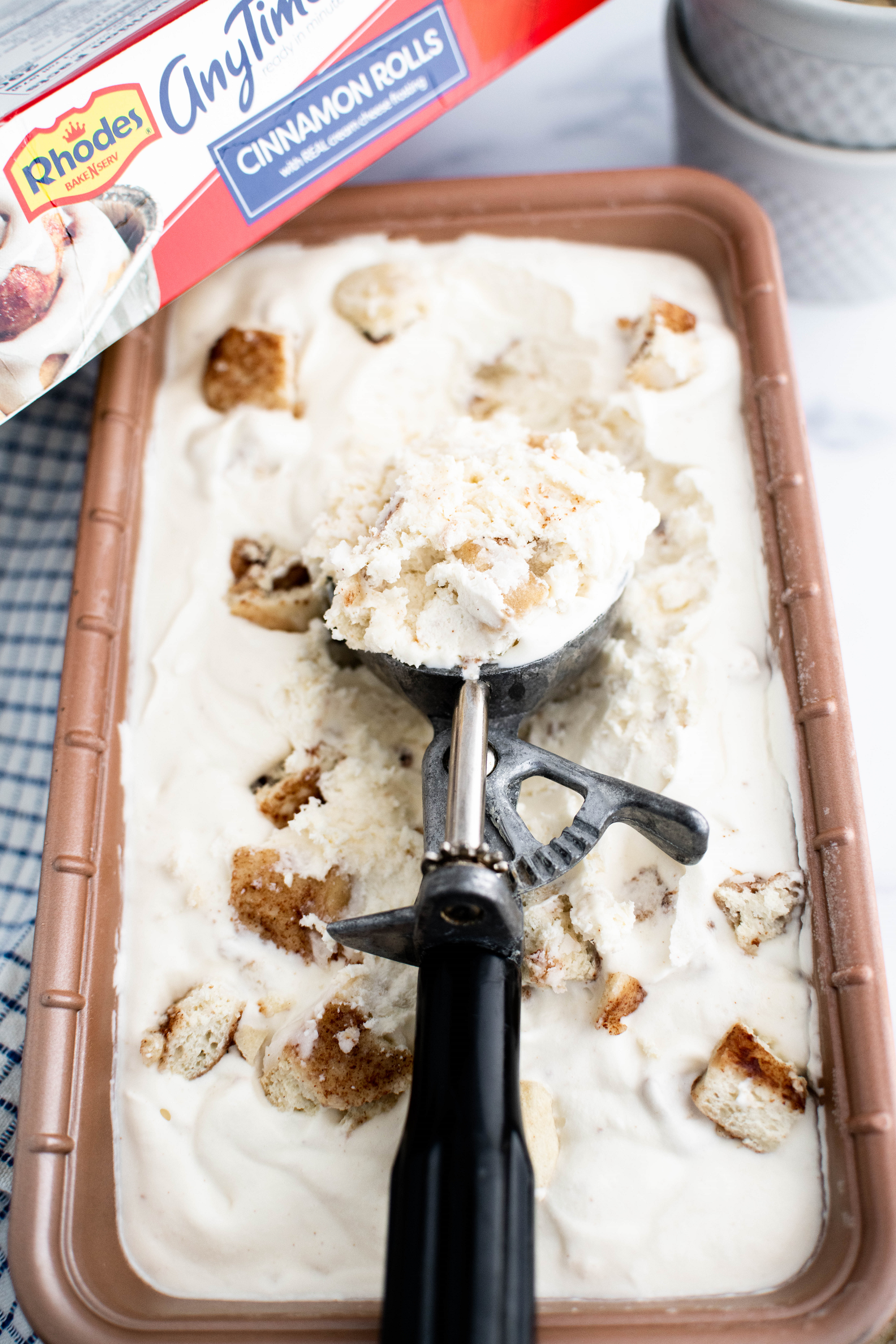 Loaf pan filled with cinnamon roll ice cream. Vintage ice cream scoop with a scoop of ice cream in it leaning in the pan.