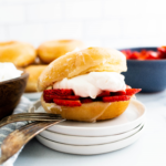 Glazed donut filled with macerated strawberries and fresh whipped cream on a small white plate.